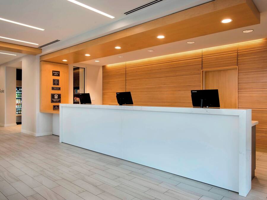 A reception desk with a white counter, wooden panel wall, and ceiling lights.