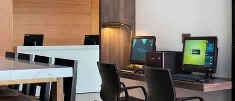 A modern office space with a reception desk, two computer monitors, and black office chairs.