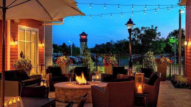Une terrasse extérieure aménagée avec des meubles en osier, un foyer, des guirlandes lumineuses et des plantes en pot.