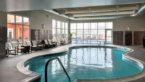 Une piscine intérieure à l’eau claire, entourée de chaises longues et dotée d’un sol carrelé.