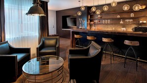 Un espace bar moderne avec une table ronde en verre, des fauteuils en cuir et un comptoir avec des tabourets.