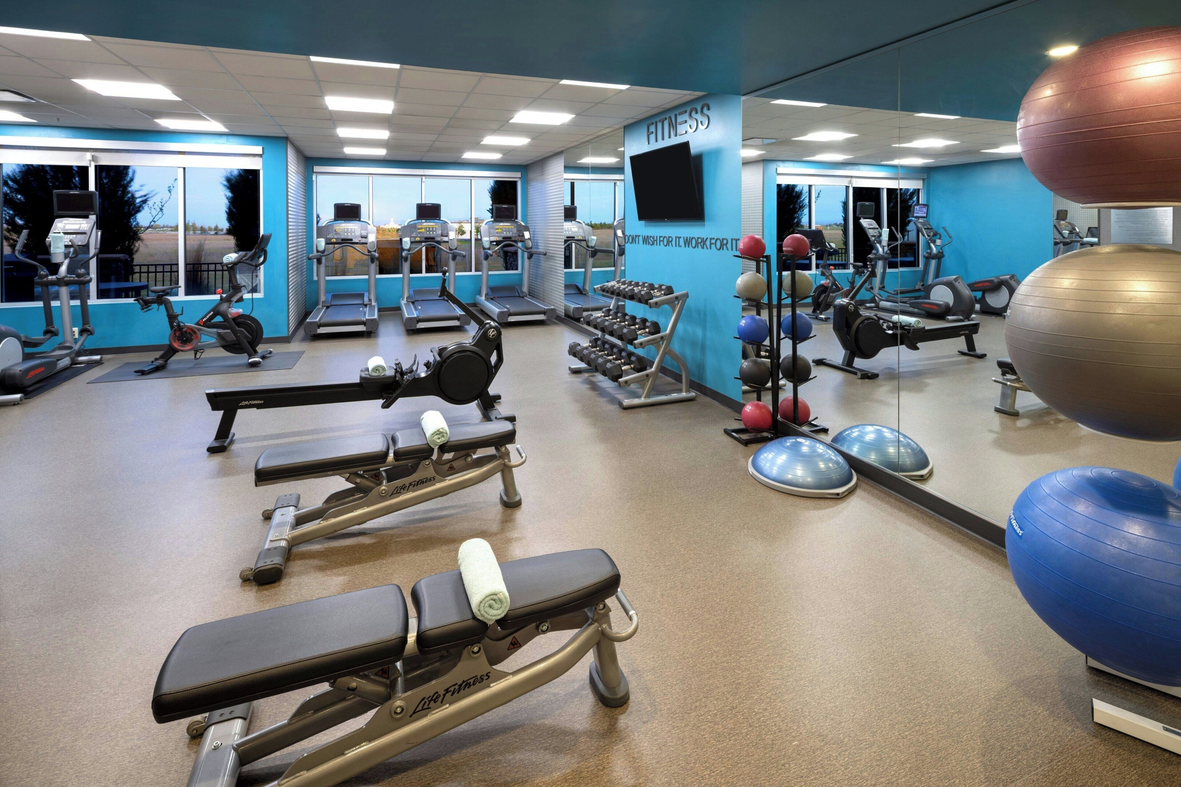 A gym with various exercise equipment, including treadmills, weight machines, and exercise balls.