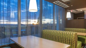 A restaurant with a view of the sunset through sheer curtains, green upholstered booths, and hanging pendant lights. - Fairfield Inn and Suites by Marriott Moses Lake (Moses Lake)