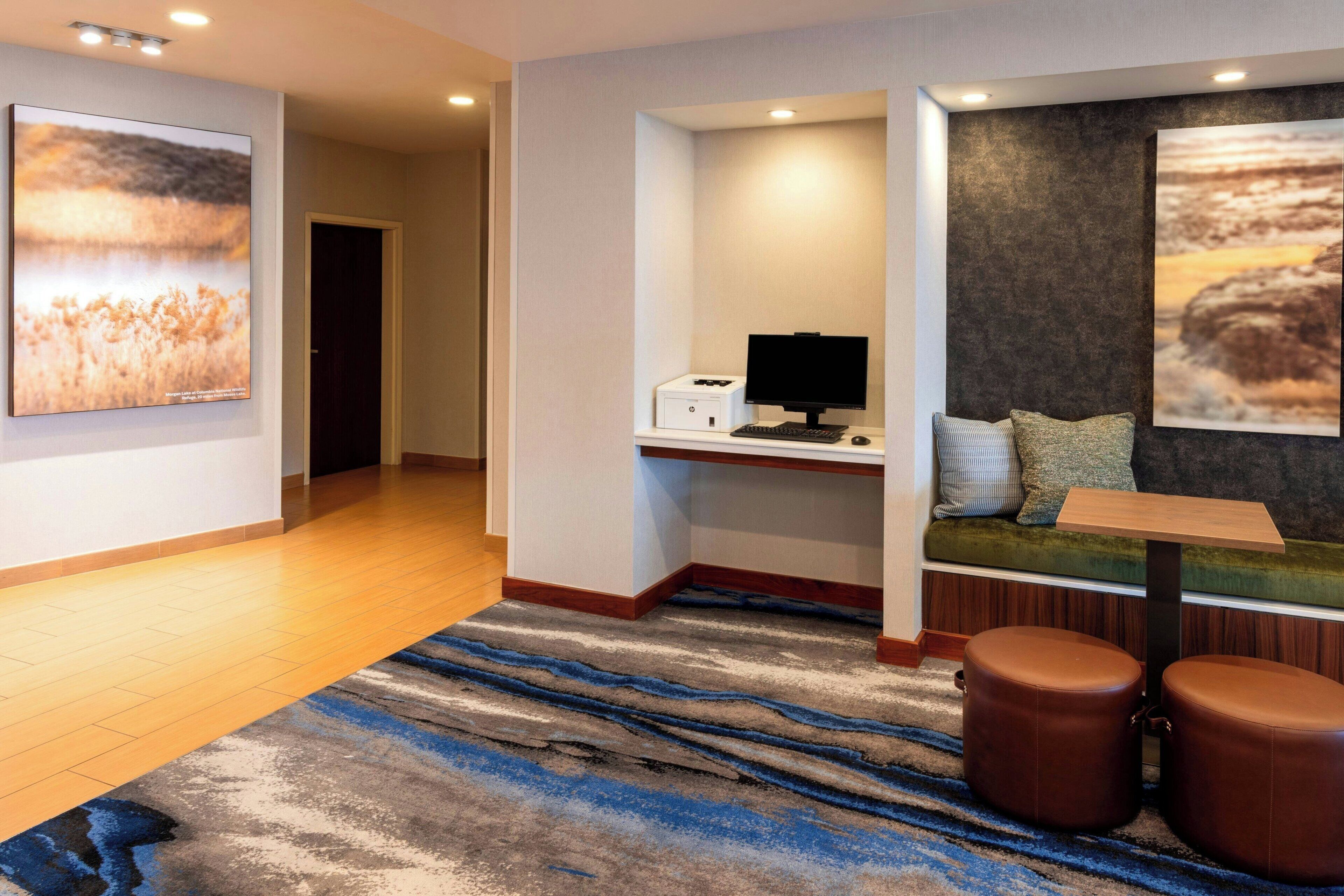 Habitación de hotel con escritorio, ordenador, zona de estar y obras de arte en las paredes.