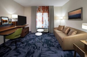A hotel room with a flat-screen TV, a sofa, a desk with a chair, a small table, and a window with curtains.