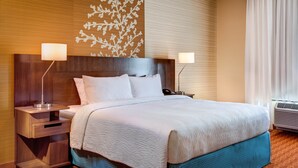 A hotel room with a large bed, two bedside lamps, a wooden headboard, a wall with a leaf pattern, and a window with curtains. - Fairfield Inn and Suites by Marriott Moses Lake (Moses Lake)