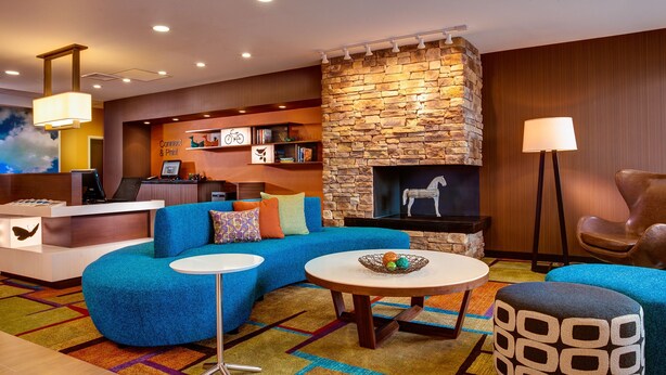 A modern living room with a stone fireplace, a blue sofa, a round coffee table, and a desk with a computer. - Fairfield Inn and Suites by Marriott Moses Lake (Moses Lake)