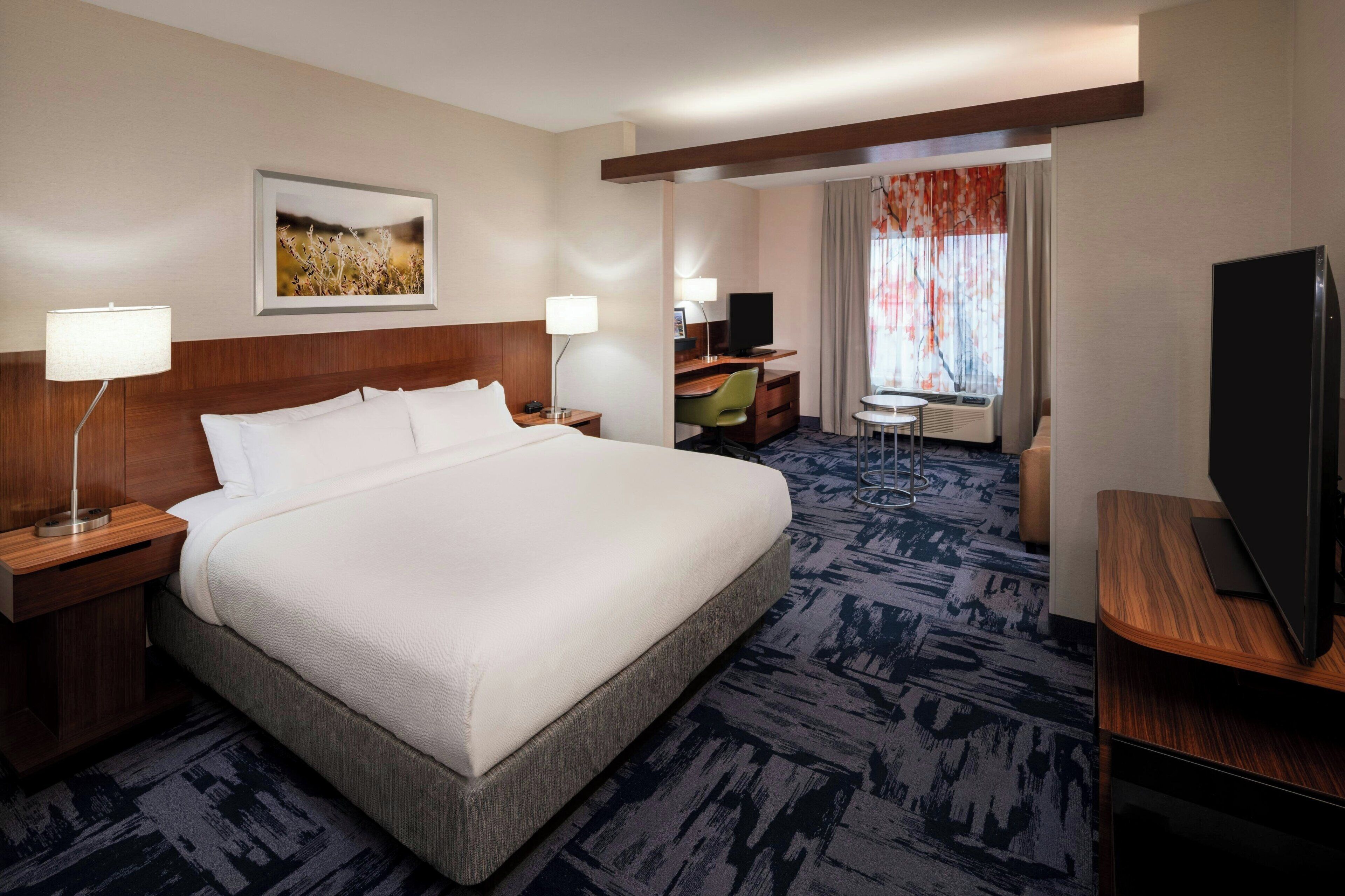 A hotel room with a large bed, a desk, a television, and a window with curtains.