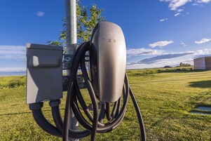 A Tesla charging station with multiple cables connected to it, set against a grassy field and a clear sky.