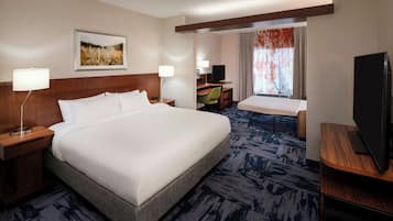 Habitación de hotel con una cama grande, un escritorio con una silla, un televisor y una ventana con cortinas.