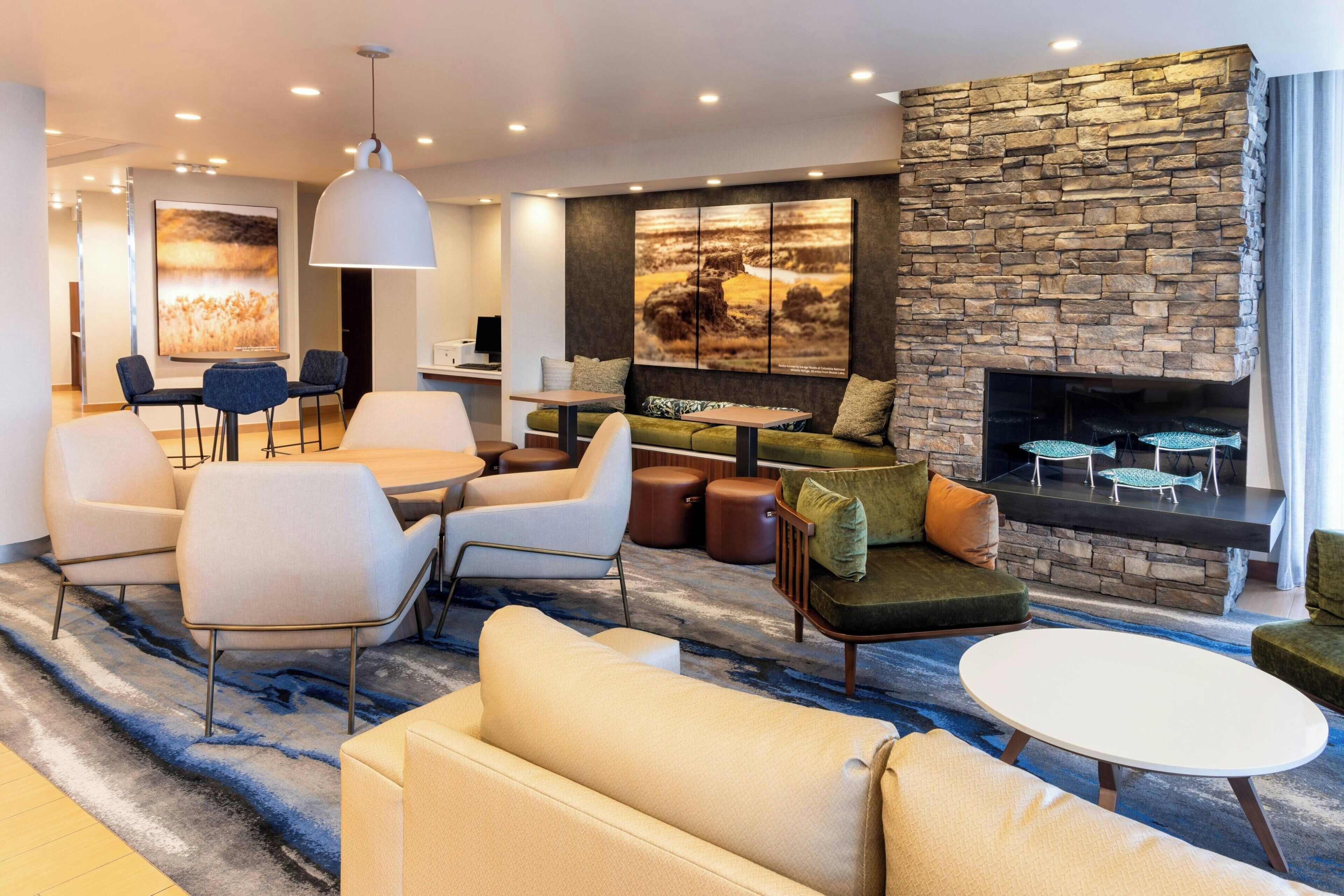 A modern hotel lobby with a stone accent wall, a fireplace, and a seating area with sofas and chairs.