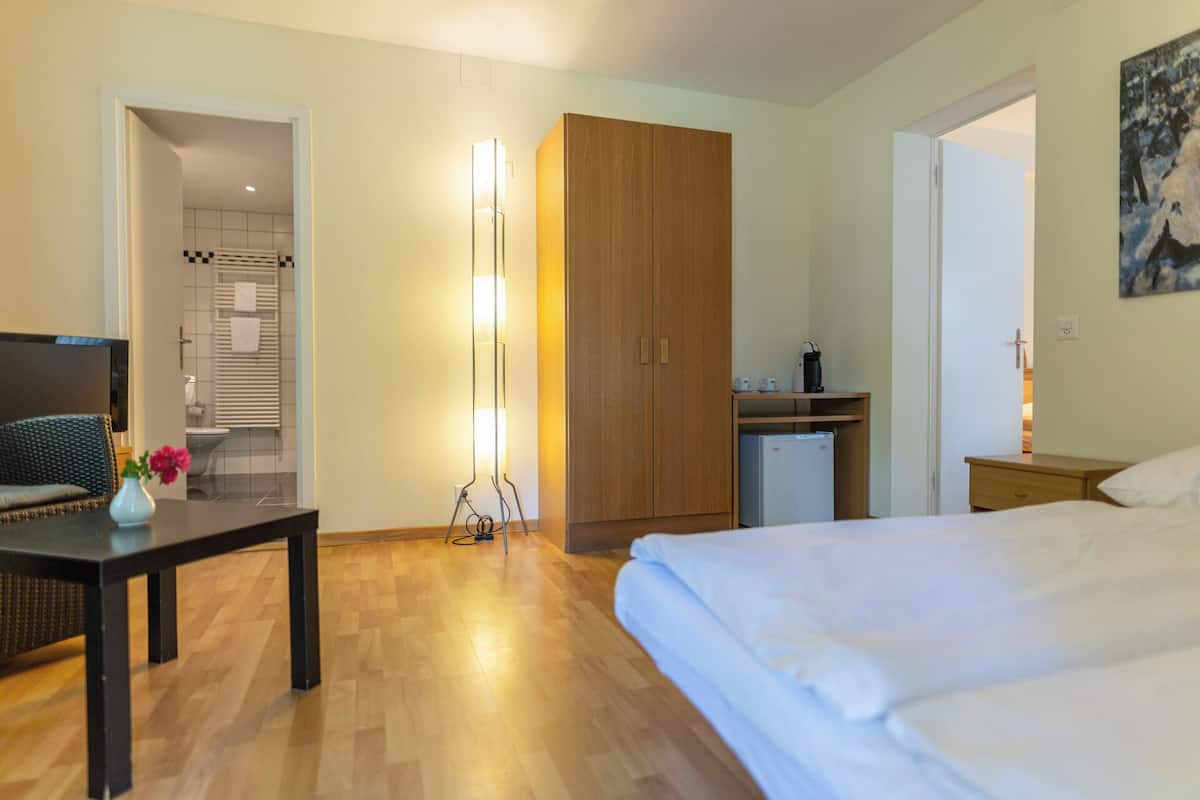 Quarto de hotel com cama, escrivaninha, armário, banheiro e um quadro na parede.