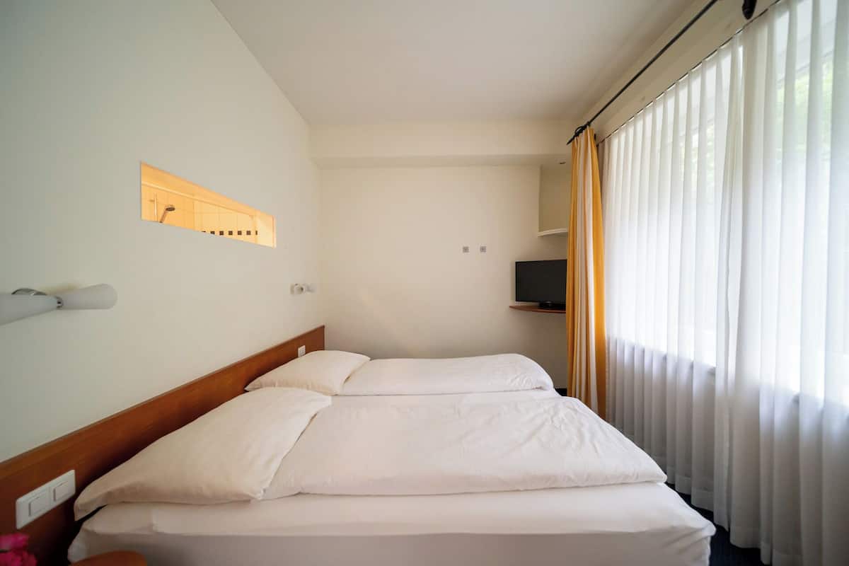 Quarto de hotel com duas camas, televisão na parede e janela com cortinas.