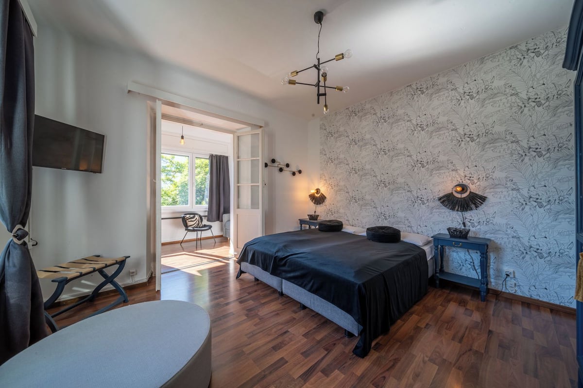 Quarto com uma cama grande, uma escrivaninha, uma cadeira e uma mesa de cabeceira com luminárias.