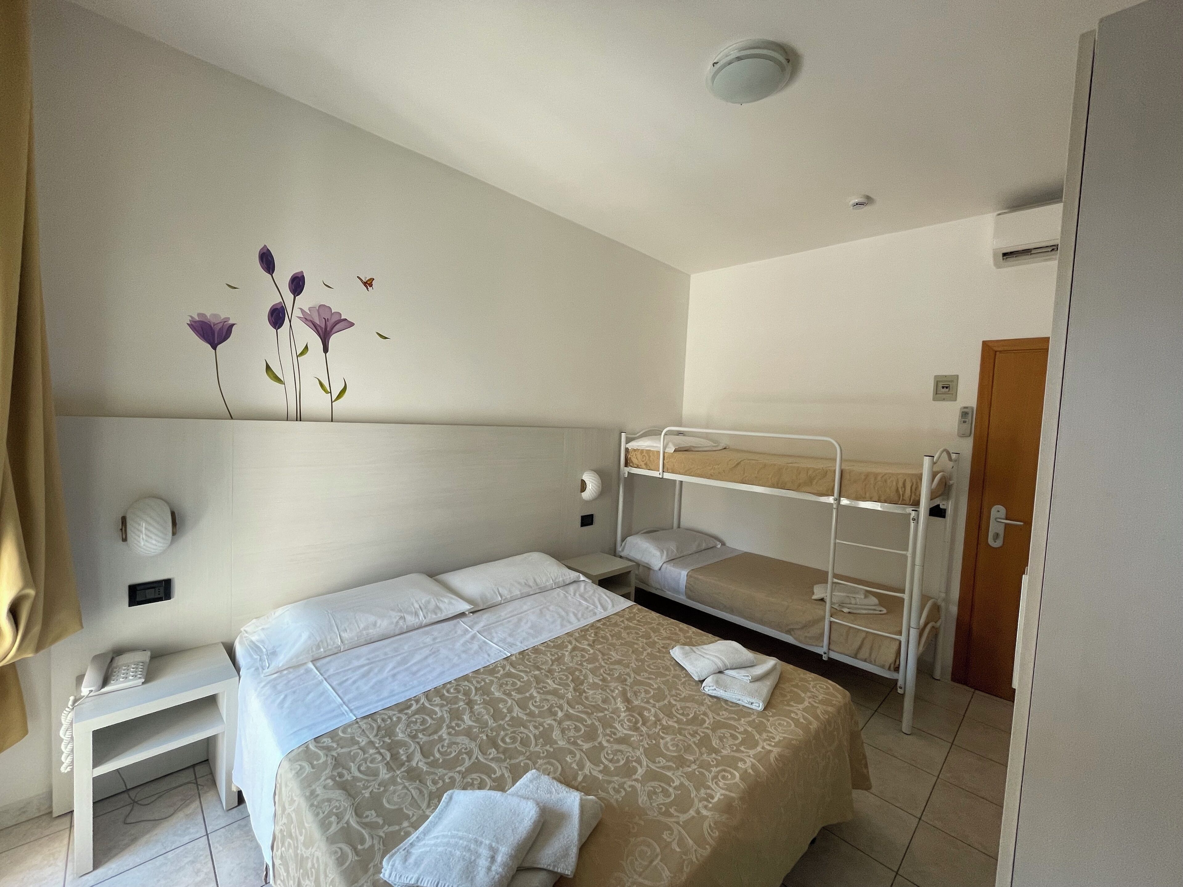 Camera d'albergo con un letto singolo, un letto a castello più piccolo, un comodino con una lampada e un telefono fissato al muro.