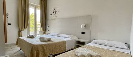 A hotel room with two beds, a bedside table, a nightstand, and a window with curtains.