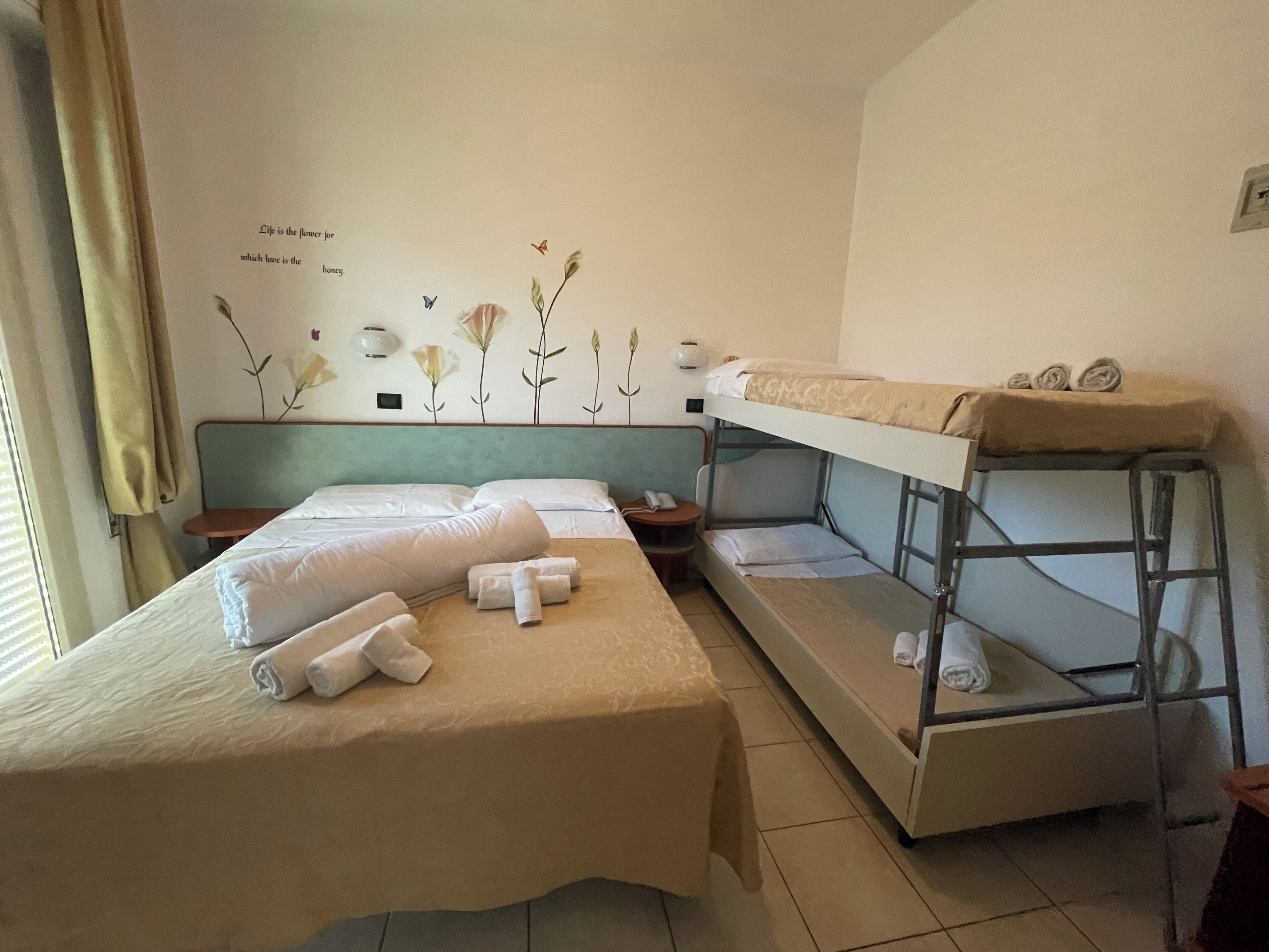 Habitación de hotel con dos camas, una de ellas con literas, y una pared decorada con un mural floral.
