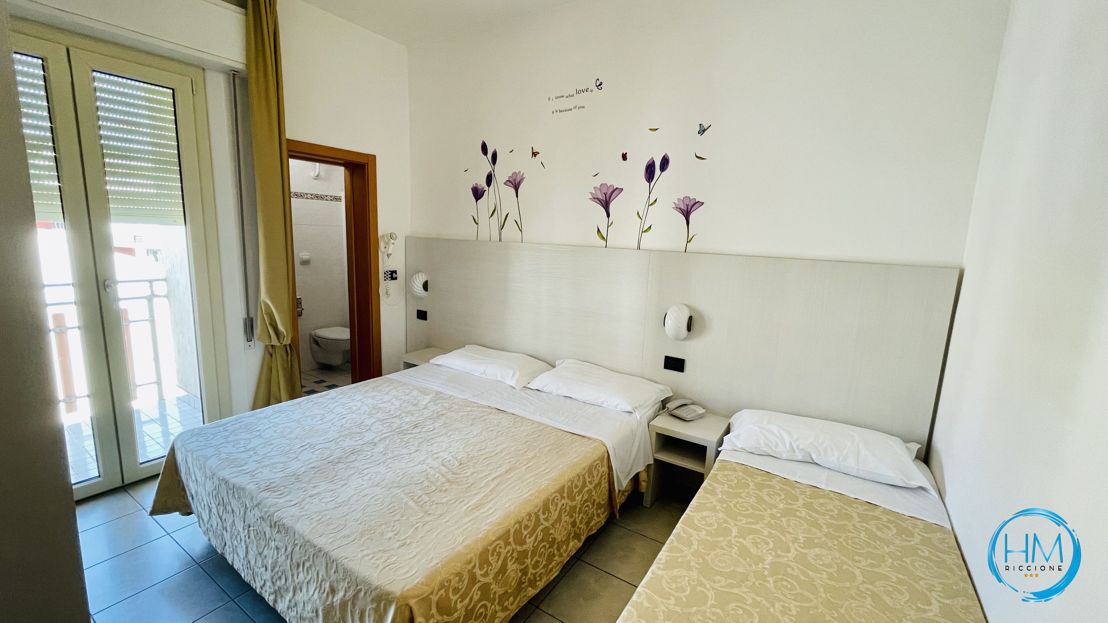 Een hotelkamer met een bed, een nachtkastje met een telefoon en een wand met een bloemendesign.