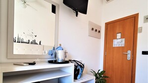 Une chambre d’hôtel compacte équipée d’un réfrigérateur intégré, d’un téléviseur à écran plat fixé au mur, d’une porte en bois et d’une plante en pot.