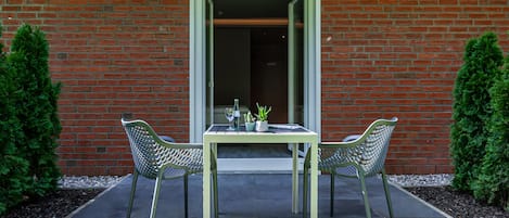 An outdoor patio with a table and two chairs, a potted plant, and a glass of water.