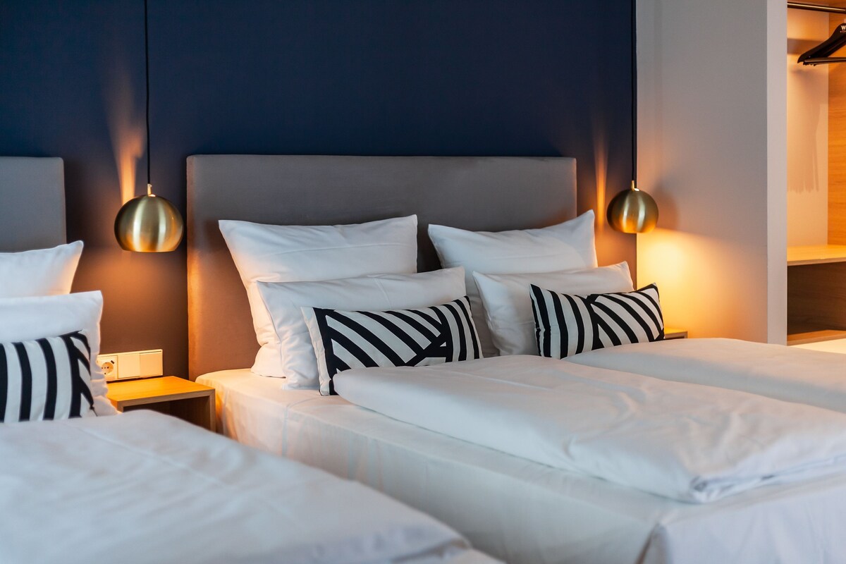 A hotel room with two beds, a headboard, bedside tables, and pendant lights.