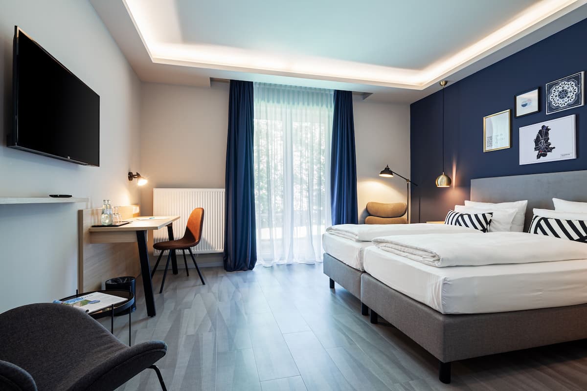 Una habitación de hotel con cama, escritorio, silla, televisor y obras de arte en la pared.