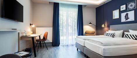 Una habitación de hotel con cama, escritorio, silla, televisor y obras de arte en la pared.