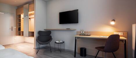 A modern hotel room with a bed, a desk with a chair, a TV, and a wardrobe with a mirror.