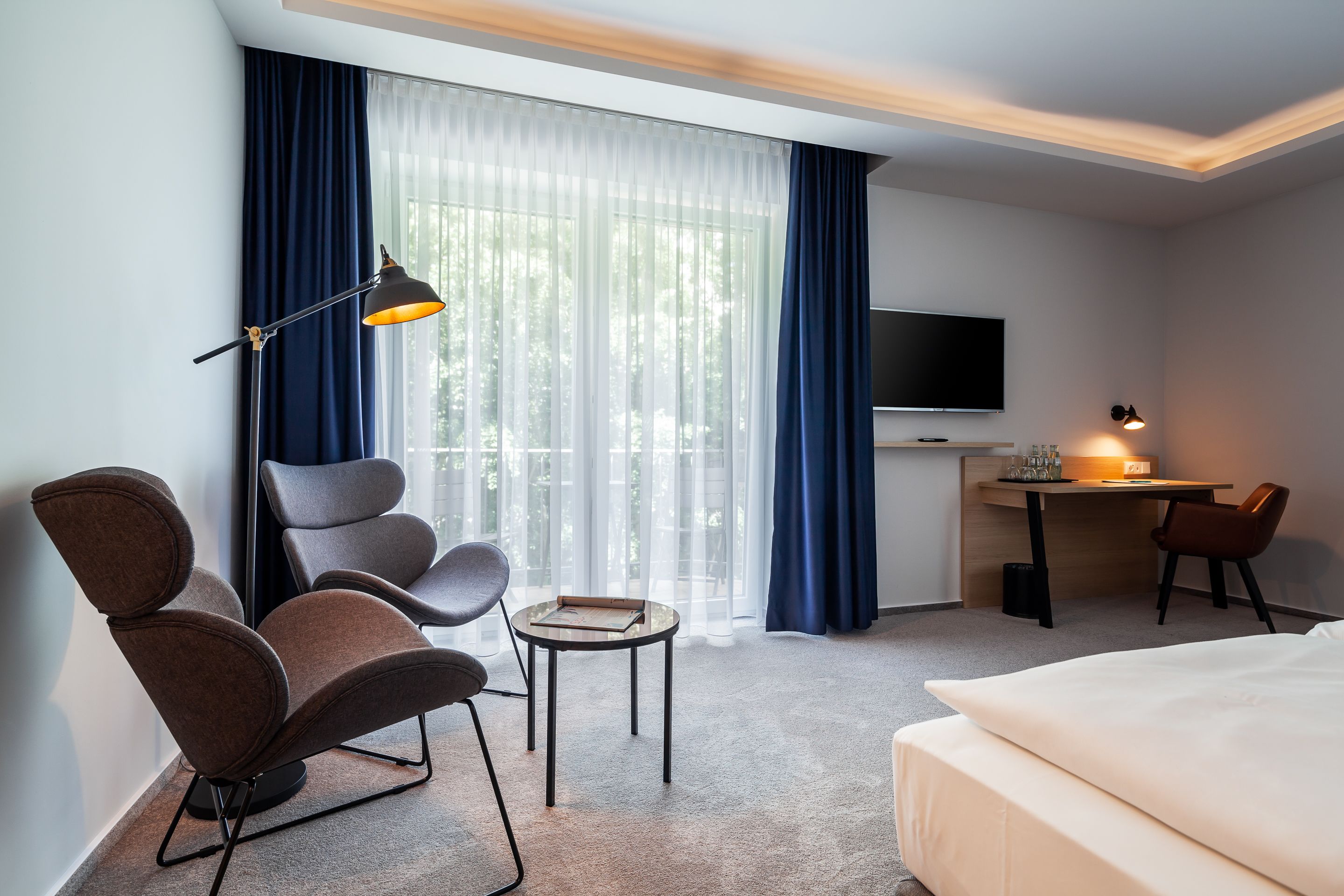 Une chambre d’hôtel équipée d’un lit, d’un bureau, d’une chaise, d’une table, d’un téléviseur et d’une fenêtre avec des rideaux.