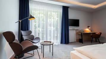 Une chambre d’hôtel équipée d’un lit, d’un bureau, d’une chaise, d’une table, d’un téléviseur et d’une fenêtre avec des rideaux.