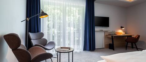 A hotel room with a bed, a desk, a chair, a table, a TV, and a window with curtains.