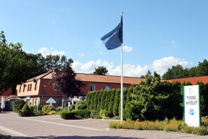 Un hotel llamado "hotel Wittorf" con un asta de bandera, un cartel de estacionamiento y un edificio rojo con tejado de tejas.
