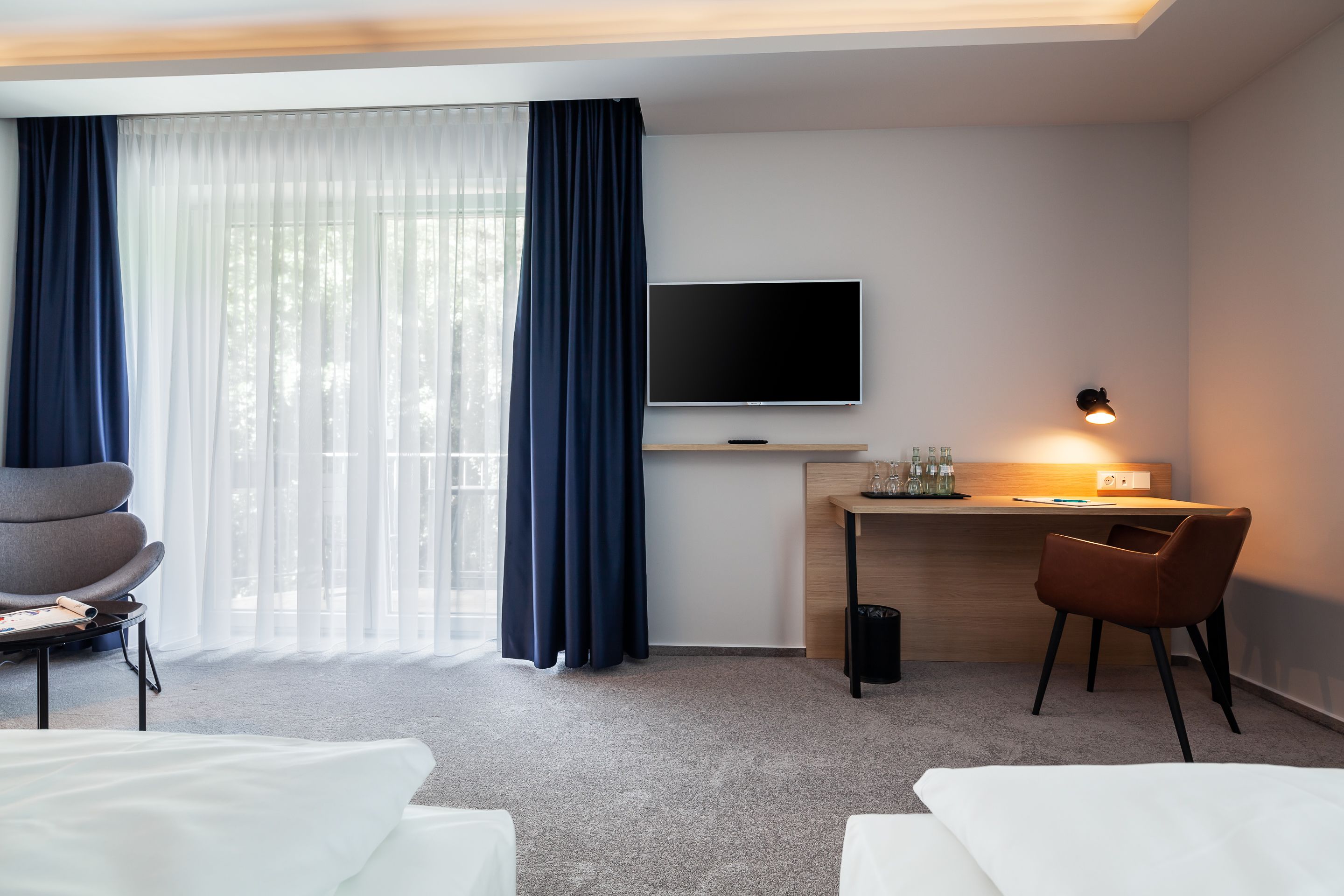 Een hotelkamer met een bed, een bureau met een televisie, een stoel en een raam met gordijnen.