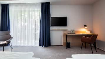 Een hotelkamer met een bed, een bureau met een televisie, een stoel en een raam met gordijnen.