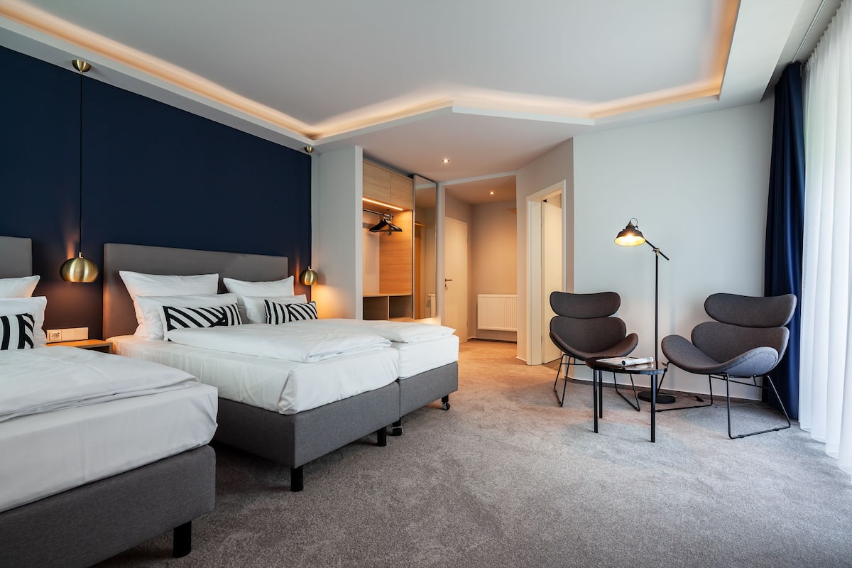Una habitación de hotel moderna con dos camas, una zona de estar y vistas al pasillo.