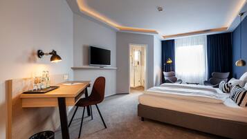 A modern hotel room with a bed, desk, chair, TV, and a bathroom door.