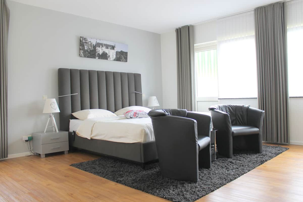 A modern bedroom with a bed, two chairs, a nightstand, and a window with curtains.