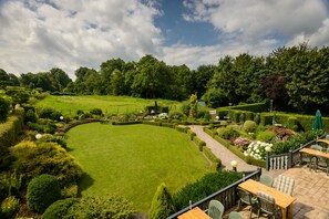 Een verzorgde tuin met een golvend gazon, strak bijgesnoeide hagen en een terras met tafels en stoelen.