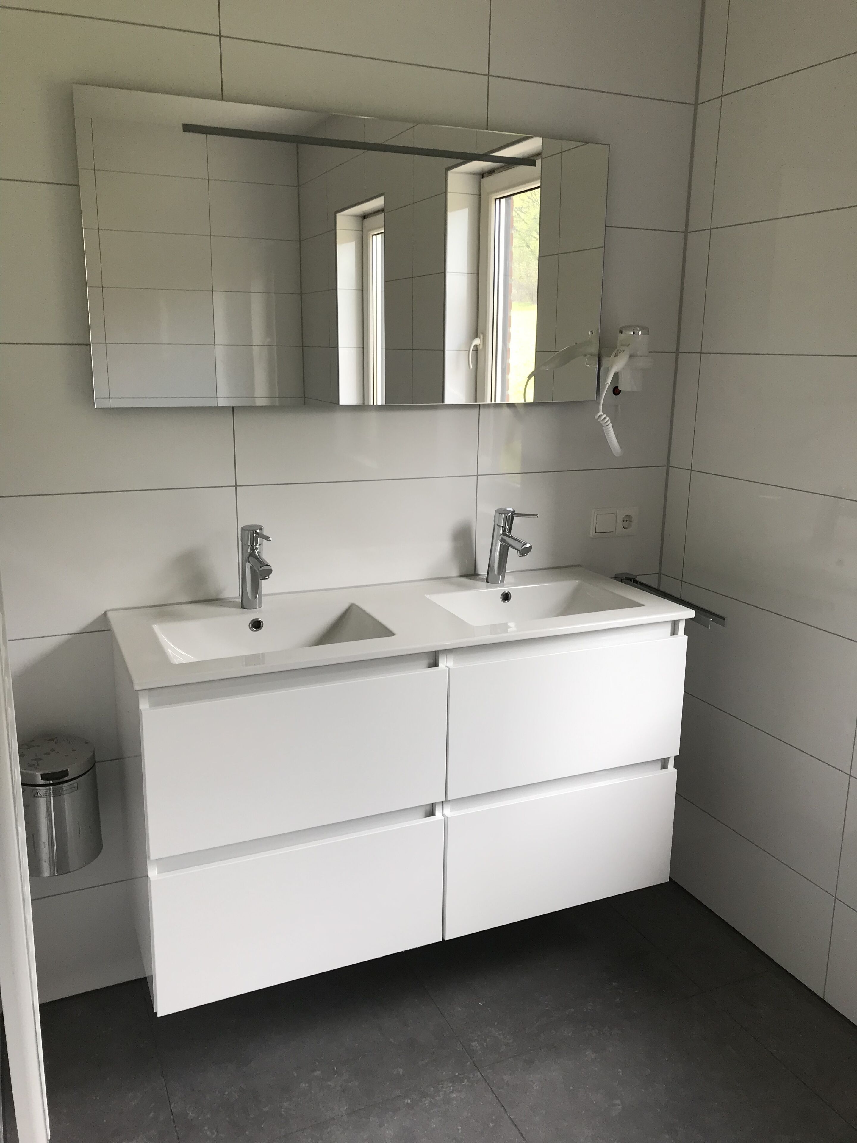Een moderne badkamer met twee wasbakken, een grote spiegel en een witte wastafel met lades.