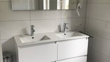 Een moderne badkamer met twee wasbakken, een grote spiegel en een witte wastafel met lades.