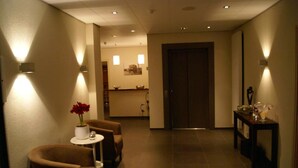 A hotel lobby with a reception desk, a seating area with two chairs and a small table, and a door leading to another room. - Hotel Bemelmans (Schin op Geul)