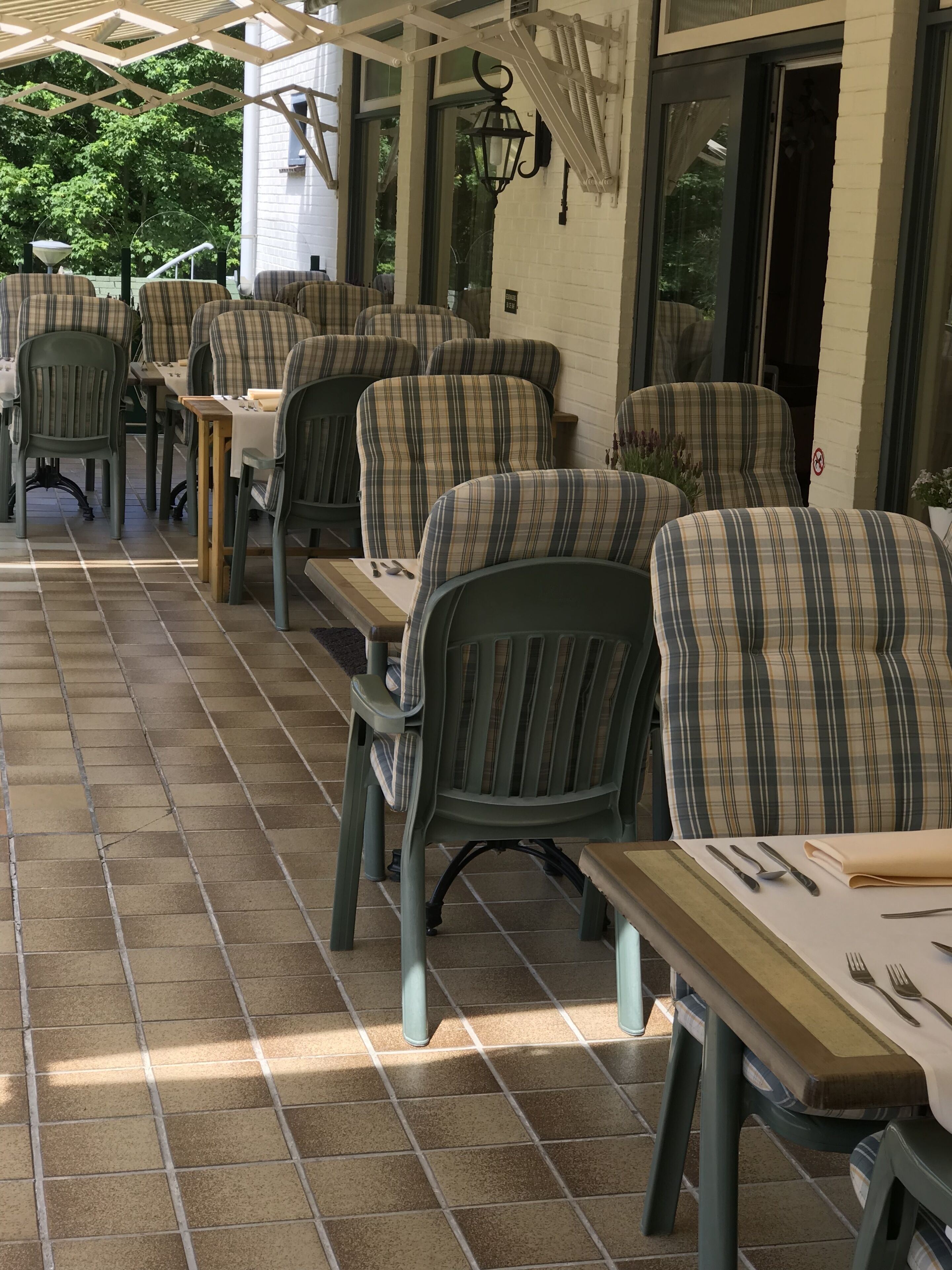 A covered outdoor seating area with multiple tables and chairs, a tiled floor, and a white brick wall.
