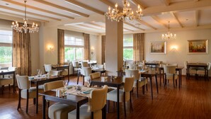 A spacious dining area with multiple tables and chairs, chandeliers, and large windows with curtains. - Hotel Bemelmans (Schin op Geul)
