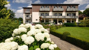 A multi-story hotel with a central courtyard, balconies, and a well-maintained garden with white flowers. - Hotel Bemelmans (Schin op Geul)