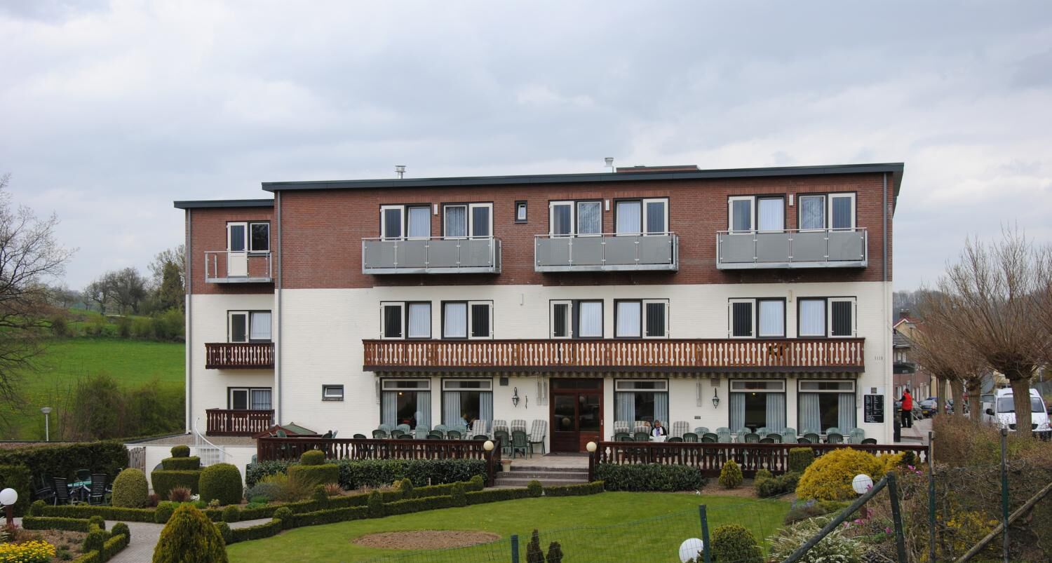 Een gebouw met twee verdiepingen, balkons, een tuin en een pad dat naar de ingang leidt.