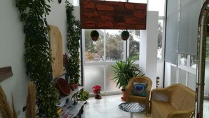 Una habitación soleada con un ventanal grande, muebles de mimbre y varias plantas en macetas.