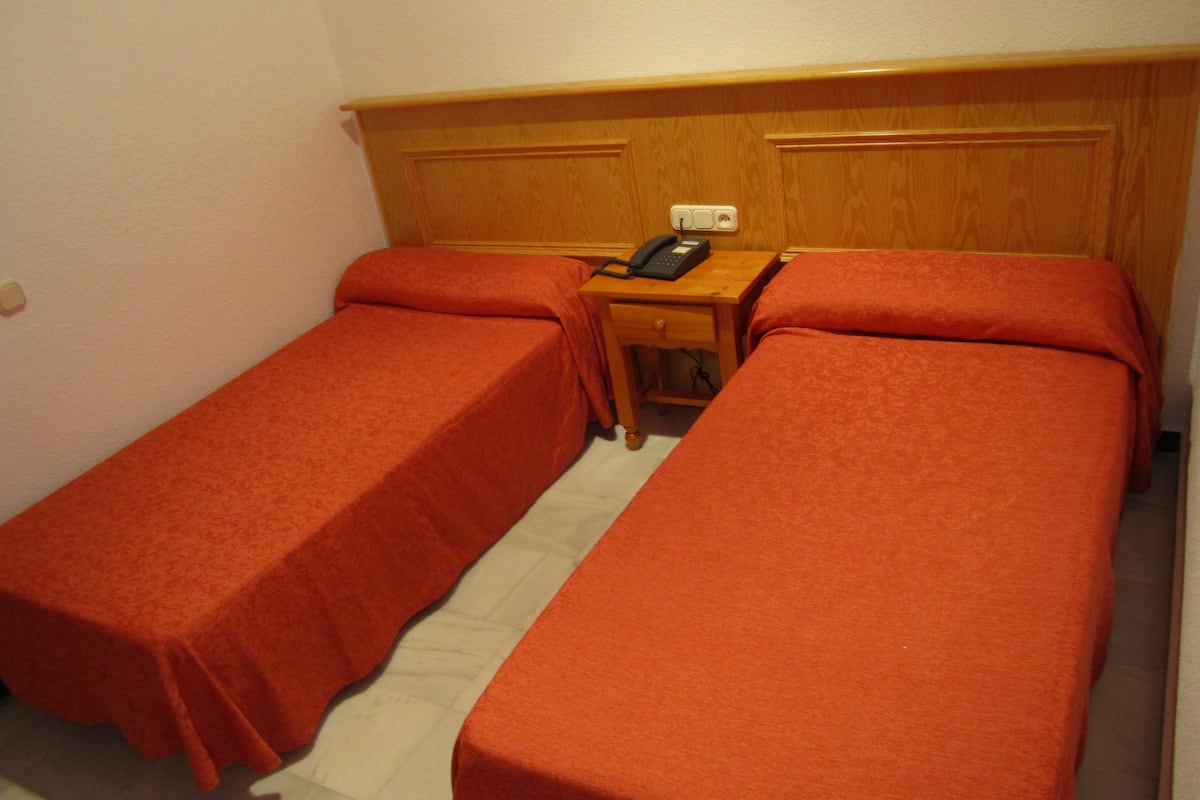 Una habitación con dos camas individuales, una mesita de noche de madera con teléfono y un enchufe.