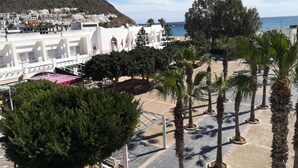 Una zona costera con edificios blancos, palmeras y una montaña al fondo.