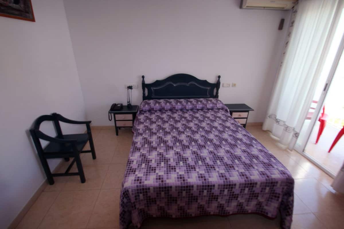 Un dormitorio con una cama, una mesita de noche, una silla y una ventana con cortinas.