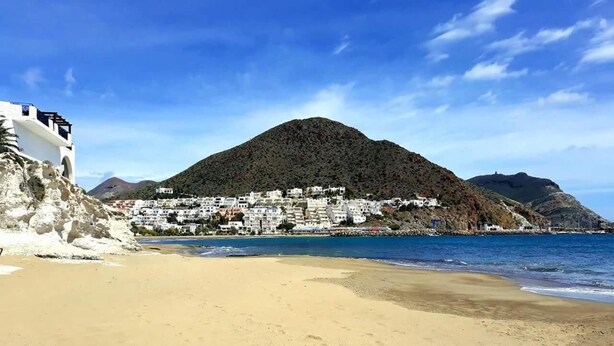 Una playa con una montaña al fondo y edificios blancos.